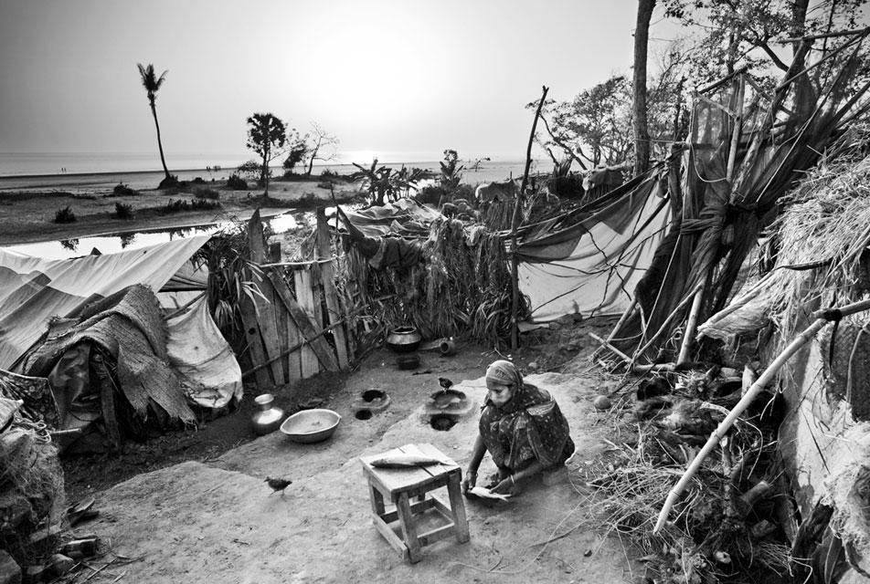 Amid a cluster of makeshift huts, a woman prepares fish for dinner. When tropical cyclone Sidr hit the coast of Bangladesh on the night of November 15, 2007, it forced thousands of people into makeshift huts constructed from whatever the storm left them. Kuakata, Bangladesh, Feb. 22, 2008.